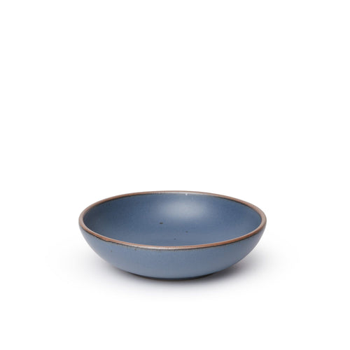 A dinner-sized shallow ceramic bowl in a cool, medium blue color featuring iron speckles and an unglazed rim