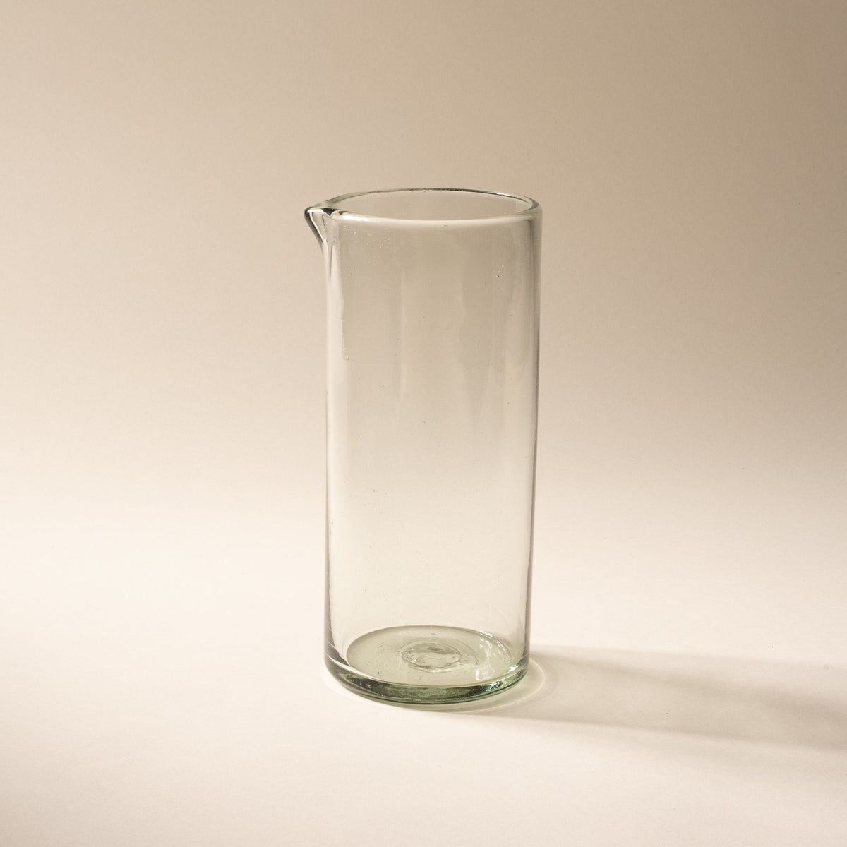A tall clear glass pitcher with small spout at the top