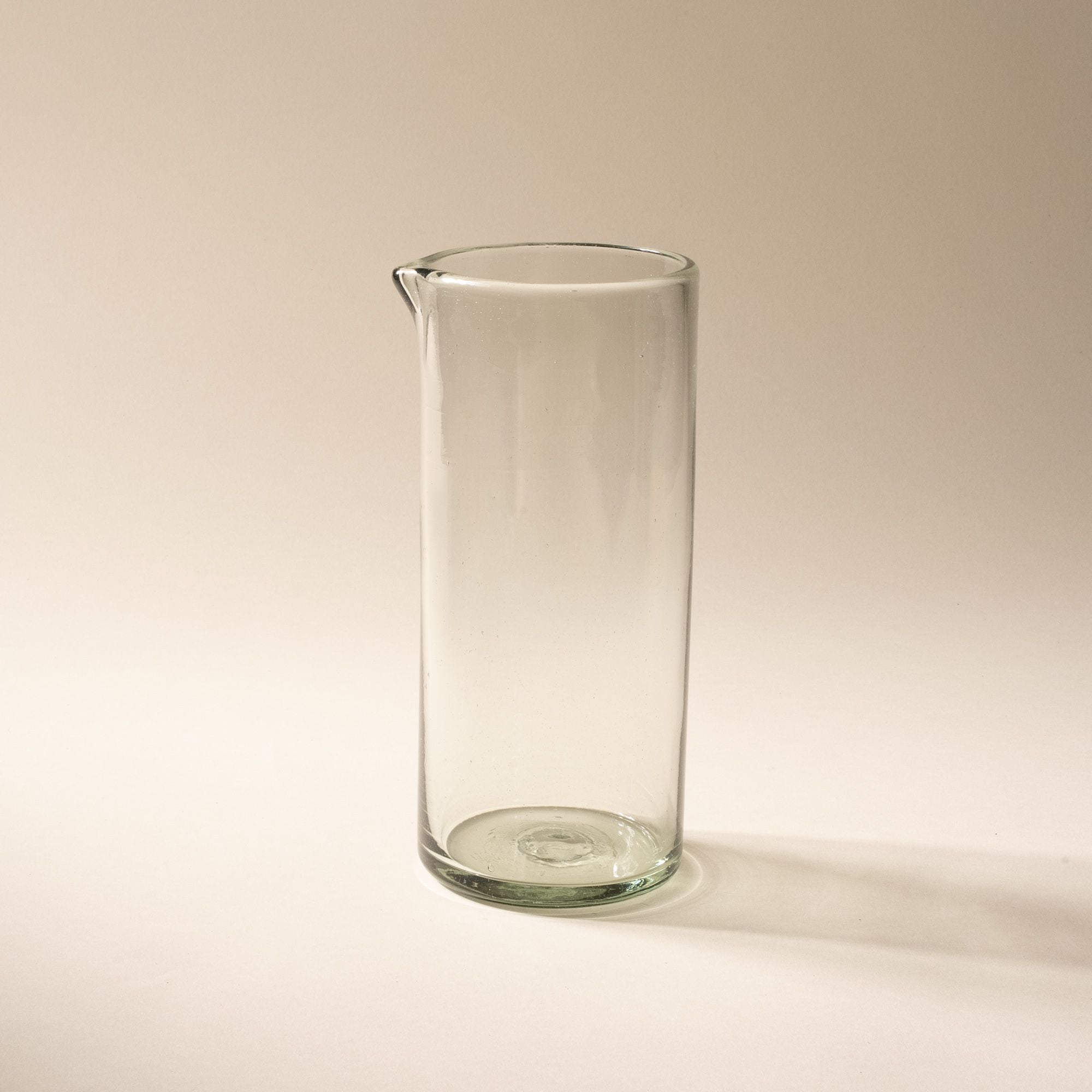 A tall clear glass pitcher with small spout at the top