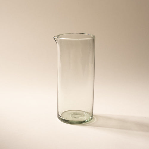 A tall clear glass pitcher with small spout at the top