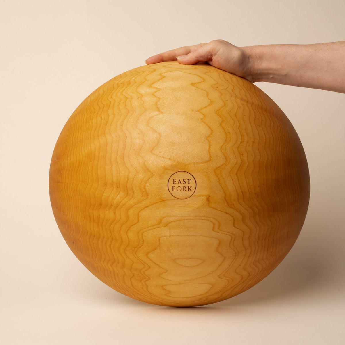 A hand holds up an extra large maple wooden bowl