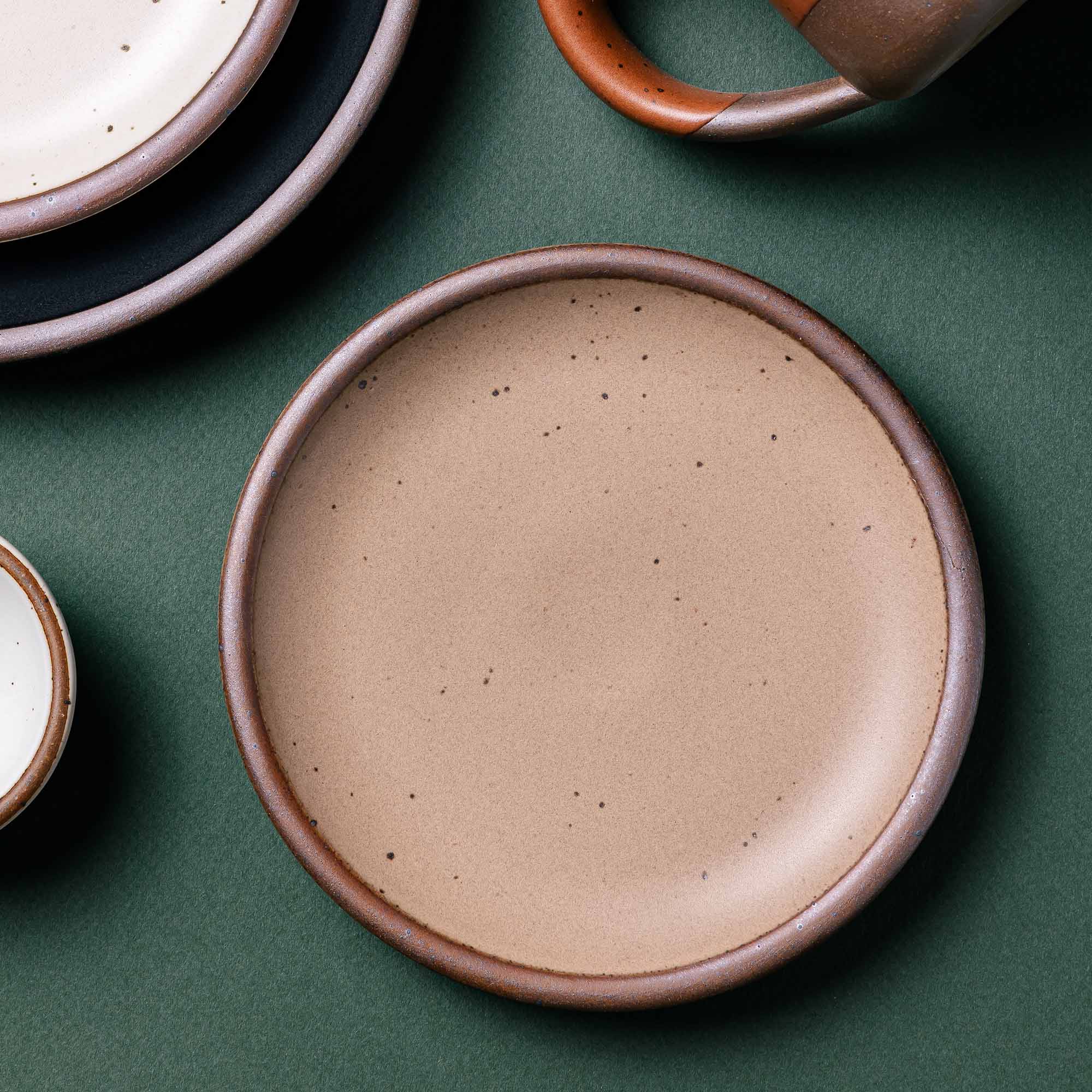 A small dessert sized ceramic plate in a cool neutral color with other pots off to the side.