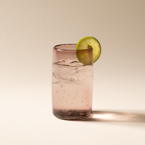 A cocktail with a lime, raspberry, and mint garnish in a light plum tall transparent drinking glass