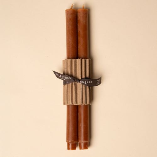 Two terracotta taper candles bundled with corrugated cardboard and tied with a black ribbon on a neutral background.