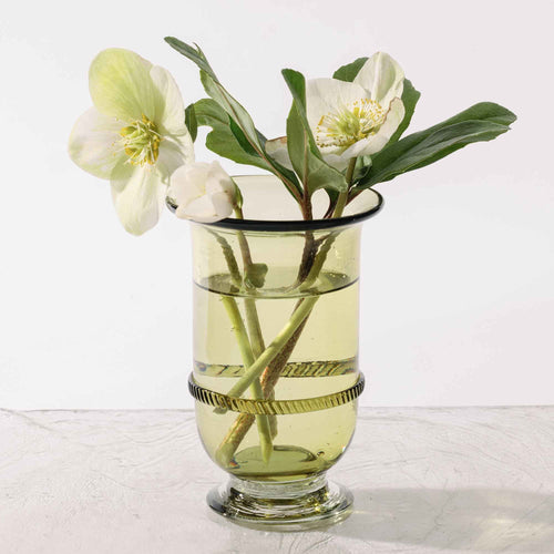 Light green glass vase with a flared rim, pedestal base, and decorative band detail at the center, filled with flower stems and water.