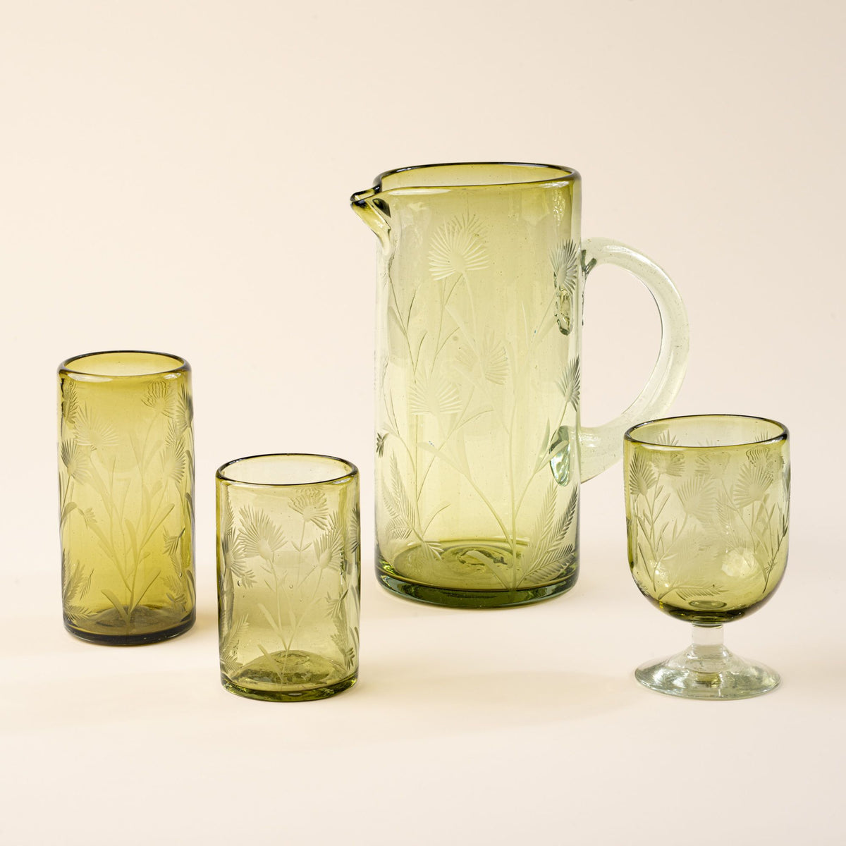 Olive tumbler, highball, wine glass and pitcher made of recycled glass with etched thistle designs on it