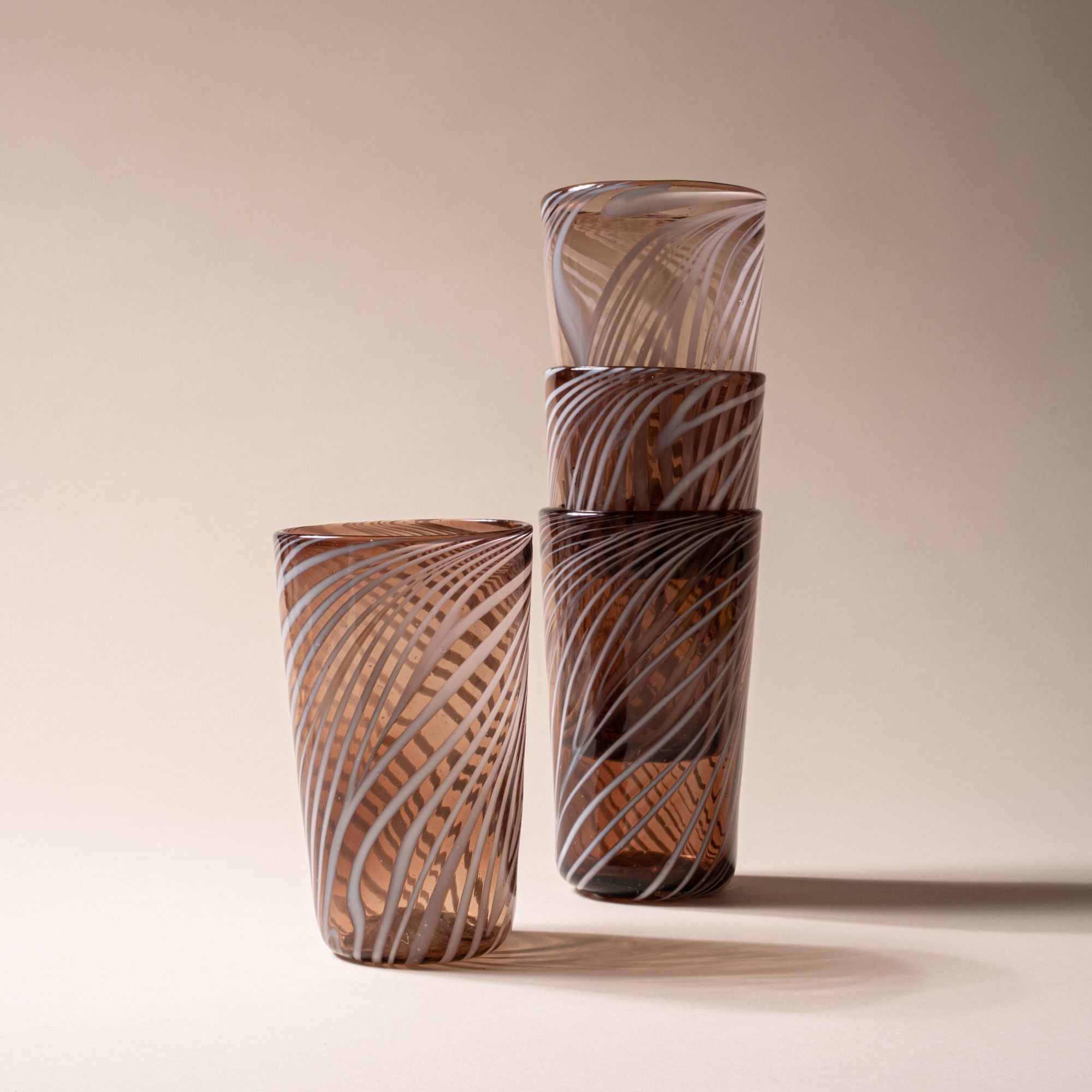 Set of four amber-toned tumblers with white swirling stripe design, three stacked and one standing beside on neutral backdrop.