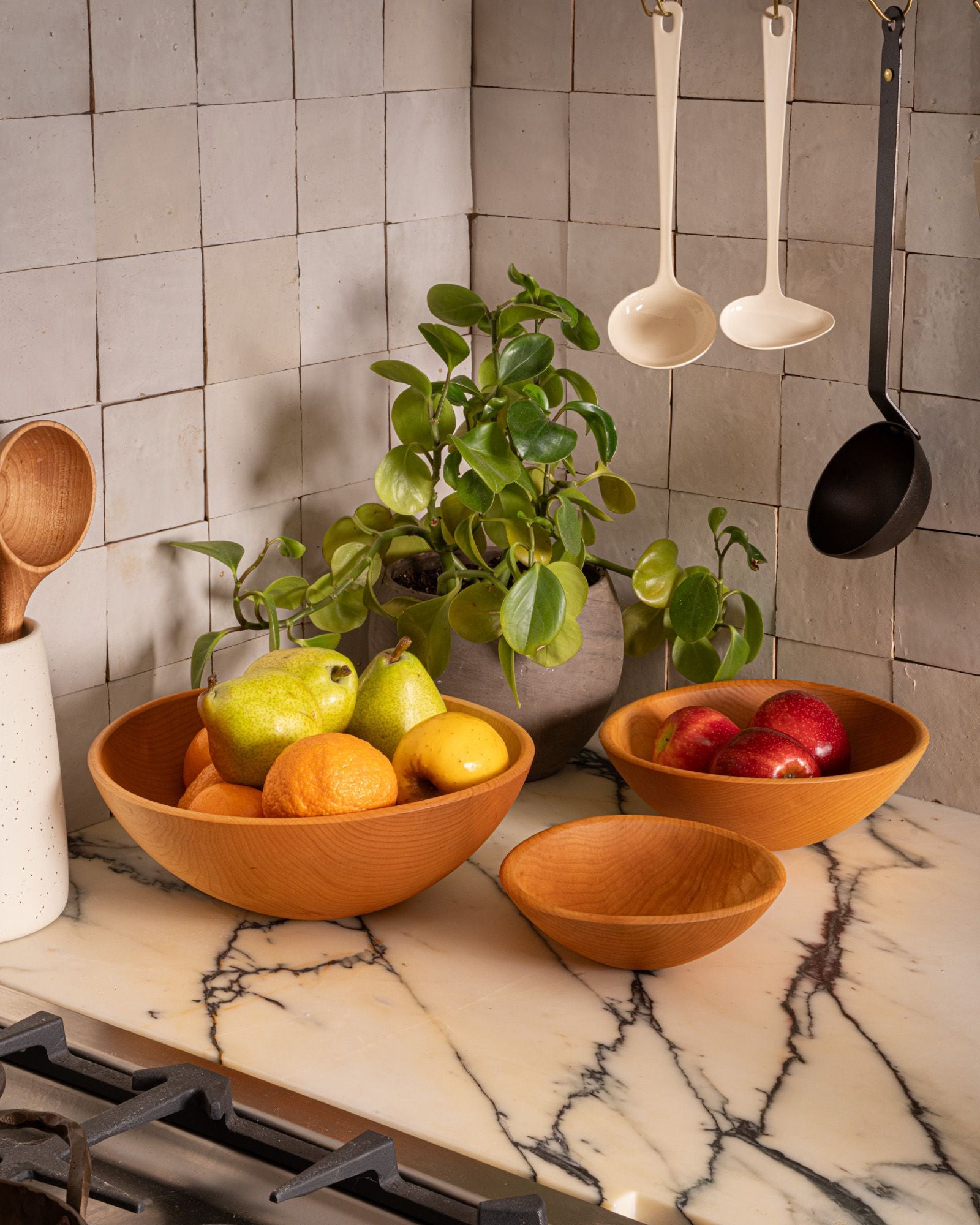 Wooden bowls filled with fresh fruit sit on a marble countertop beside a leafy potted plant in a warm, inviting kitchen scene.