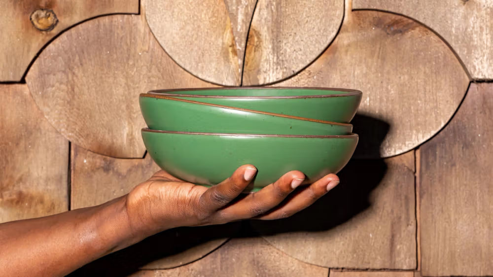 A hand holds a stack of bowls in a true green color with an unglazed rim.