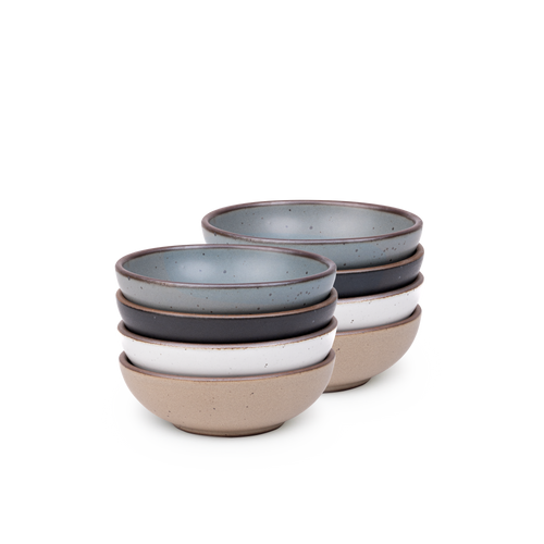 A stack of 8 small shallow ceramic bowls in a blue-grey, graphite black, cool white, and warm pale brown colors featuring iron speckles and an unglazed rim
