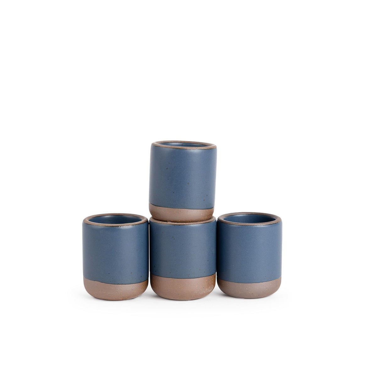 A set of 4 small, short ceramic mug cups in a cool, medium blue color featuring iron speckles and unglazed rim and bottom base, stacked in a row of 3, with the 4th on top.