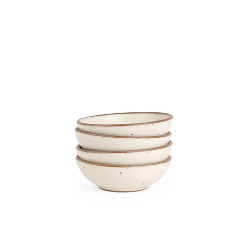 A stack of 4 small shallow ceramic bowls in a warm, tan-toned, off-white color featuring iron speckles and an unglazed rim