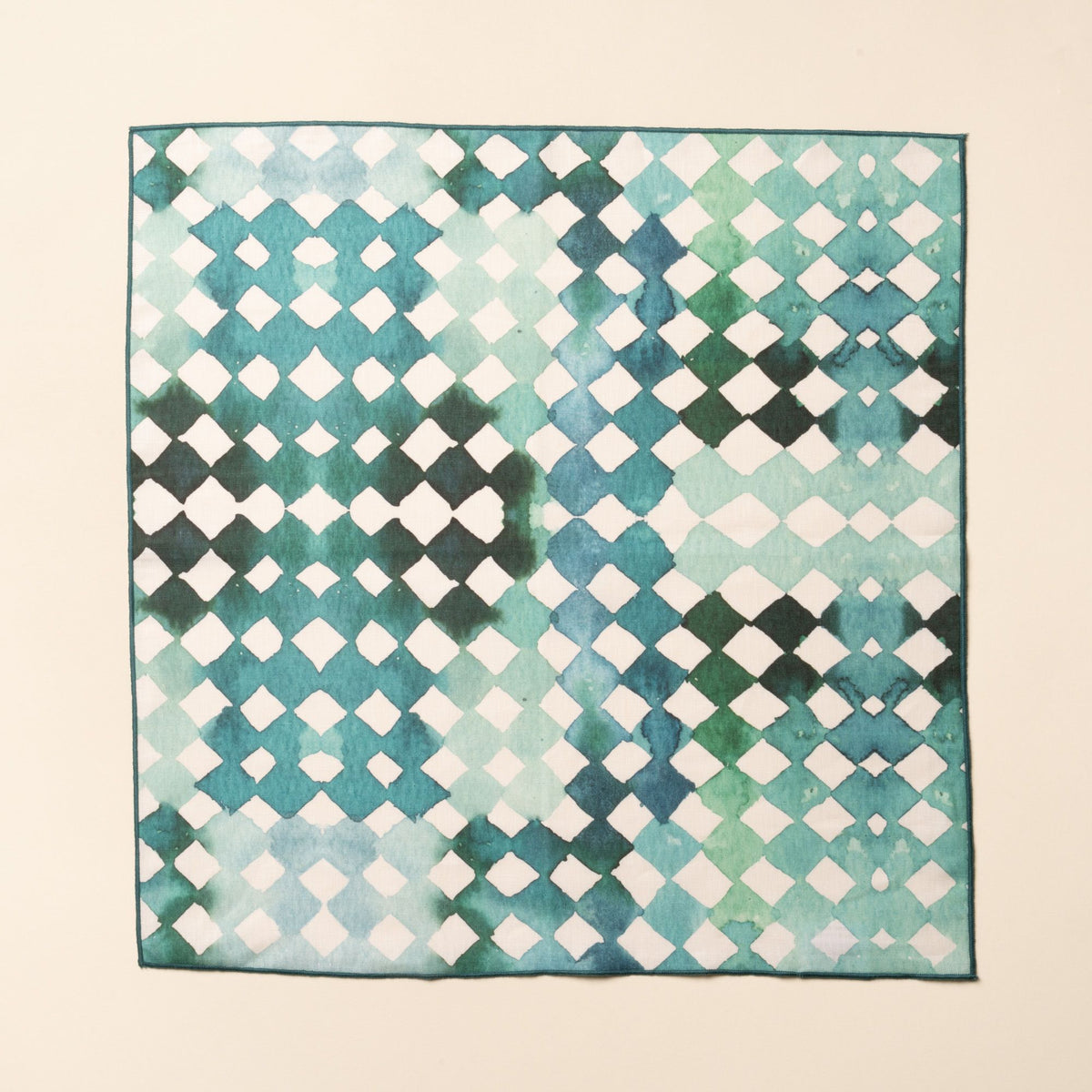 A flat square watercolor diamond-patterned cloth napkin in green and teal tones