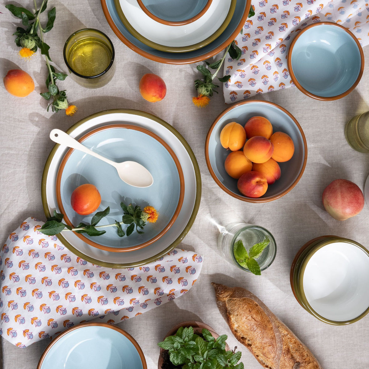 An overhead view of enamel plates and bowls in white and robin's egg blue, with food, glassware, printed napkins, and more.