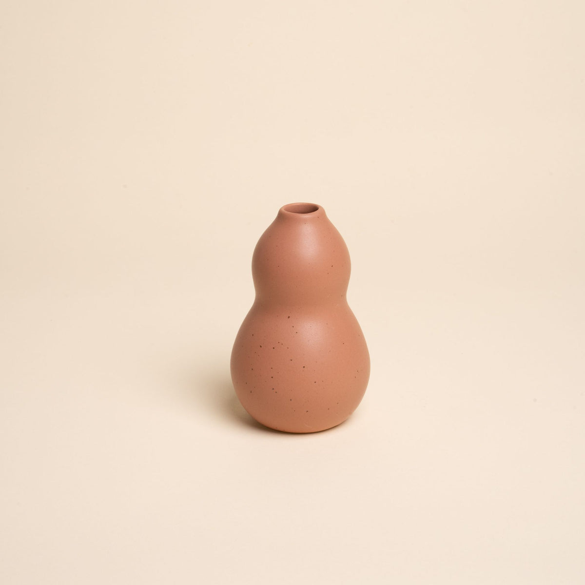 Small light terracotta ceramic vase with a curvy shape and subtle speckles, set against a soft beige background.
