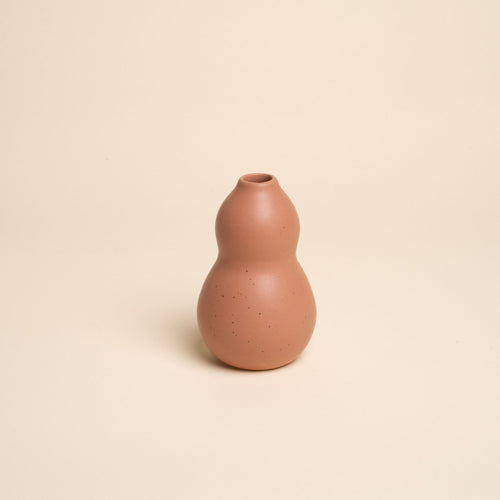 Small light terracotta ceramic vase with a curvy shape and subtle speckles, set against a soft beige background.