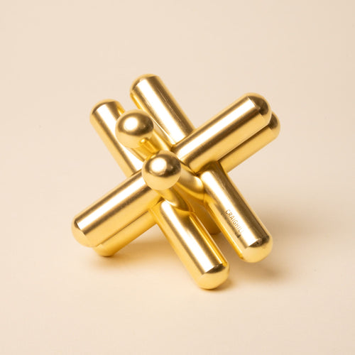 Shiny gold interlocking metal puzzle sculpture with smooth cylindrical pieces on a beige background.