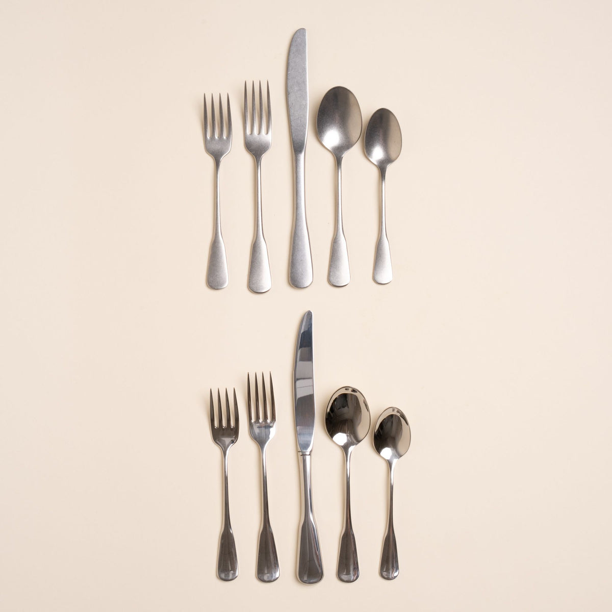 Two sets of stainless steel five-piece flatware including 2 forks, 2 spoons, and 1 knife. One is in a polished finish, the other in a tumbled matte finish, both a classic design