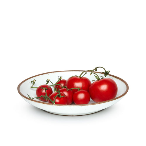 Tomatoes on a large ceramic plate with a curved bowl edge in a cool white color featuring iron speckles and an unglazed rim.