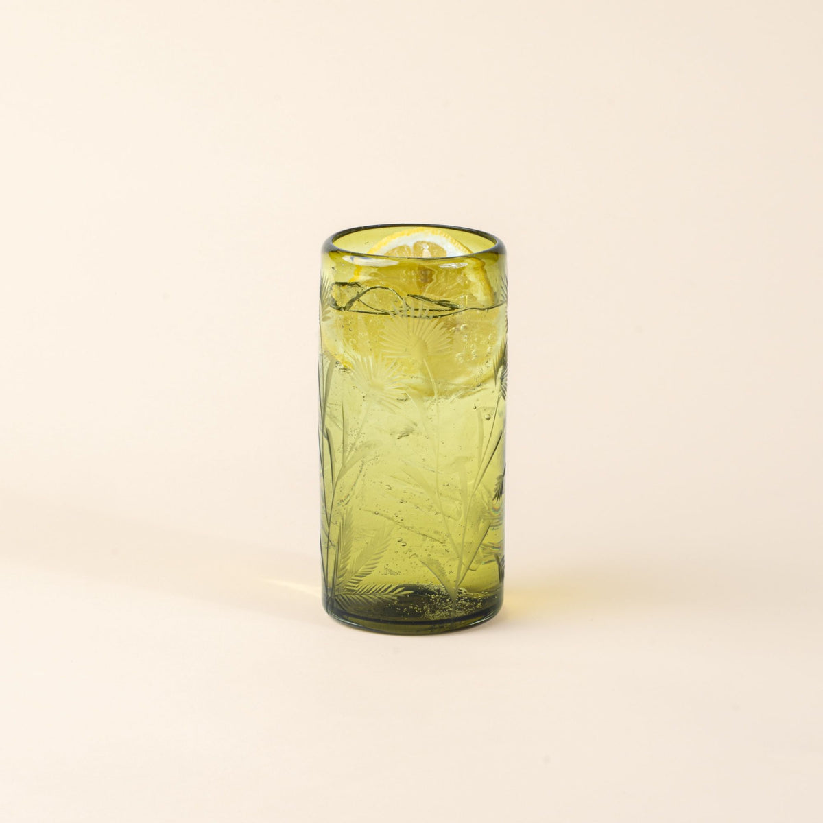 Olive cylindrical glass with delicate etched floral pattern, filled with water and a slice of lemon, standing upright on a neutral background.