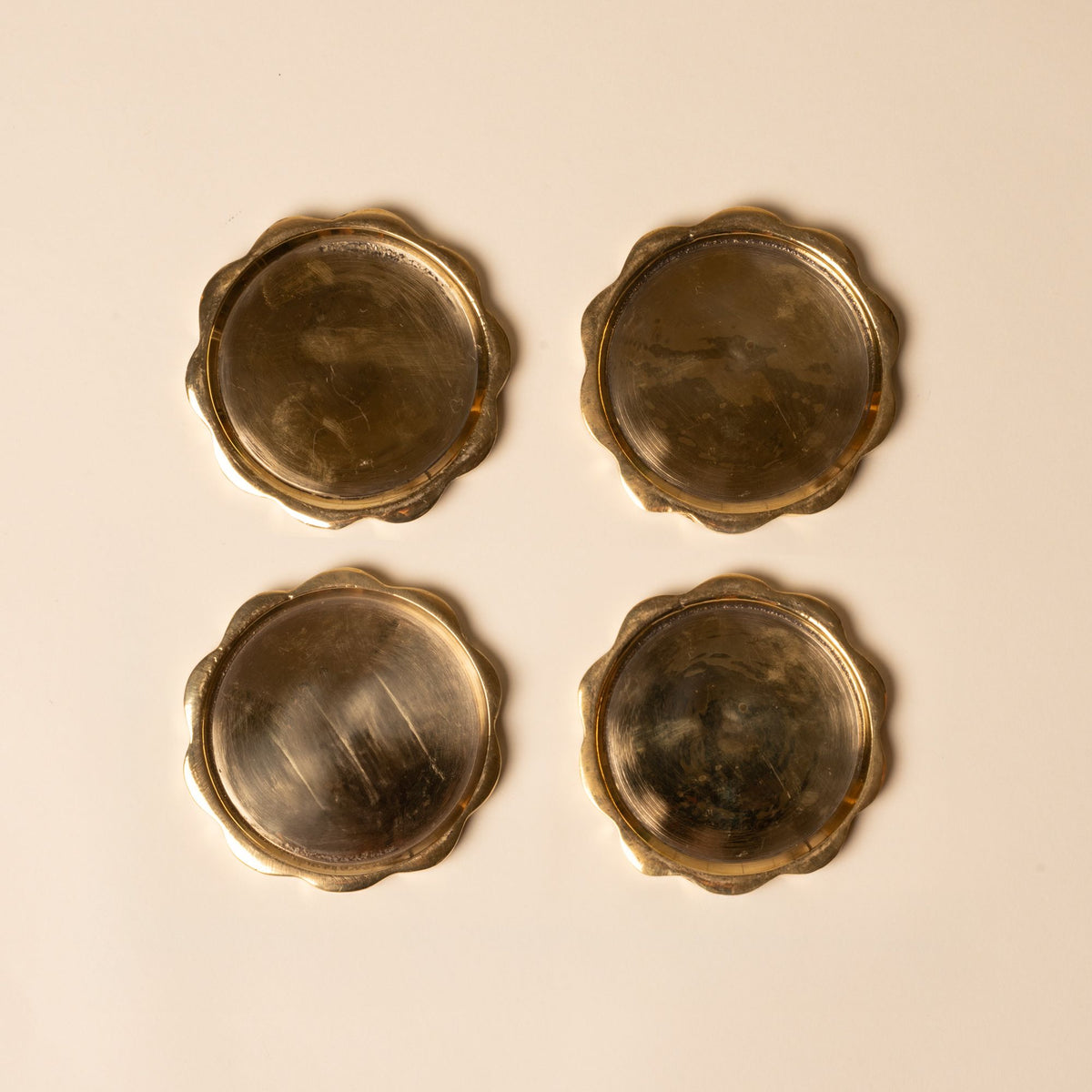 Set of four round brass coasters with scalloped edges, polished finish, and vintage patina.