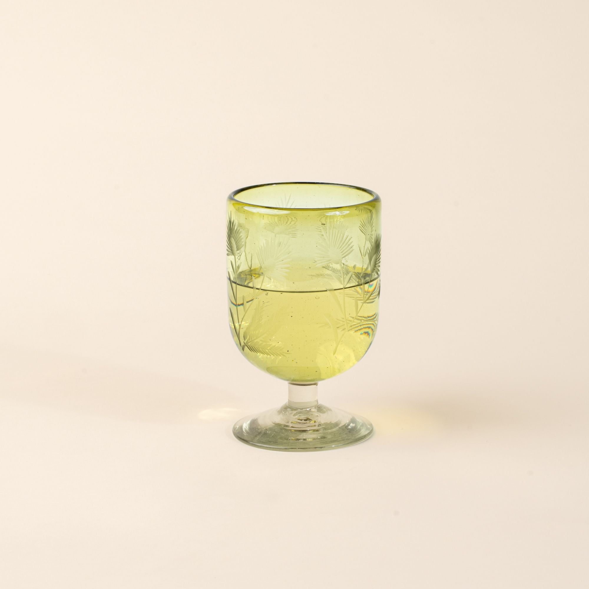 An olive short wine glass made of recycled glass with etched thistle designs on it, filled with white wine.