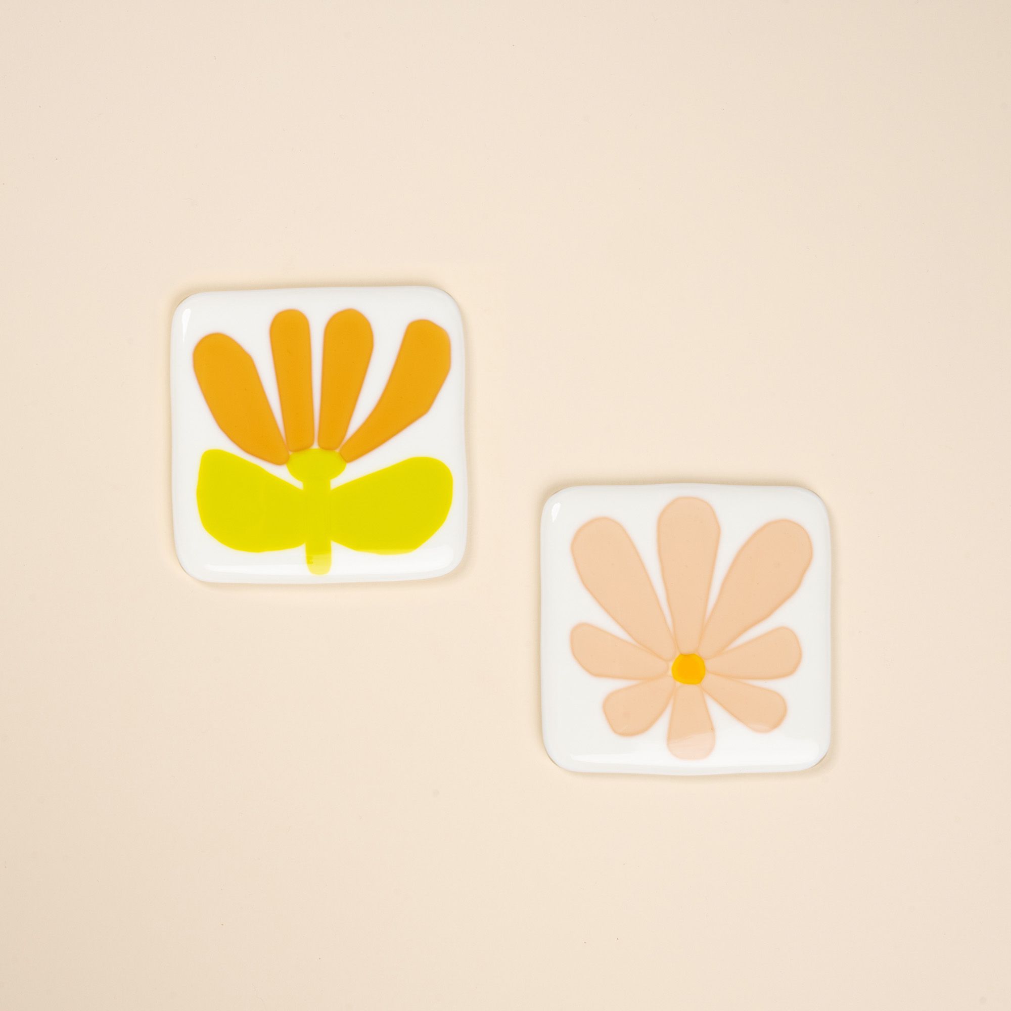 A pair of glass flower coasters, painterly simple floral shapes in peach, amber, and neon green