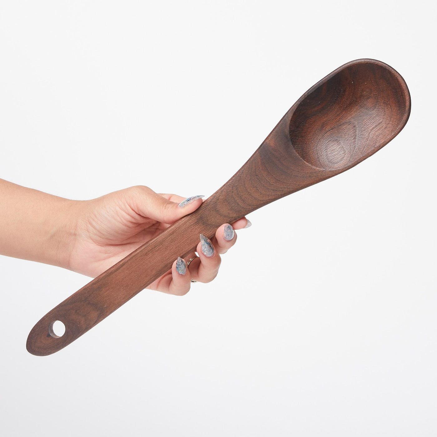 Hand holding a long black walnut wood spoon with a hole at the bottom