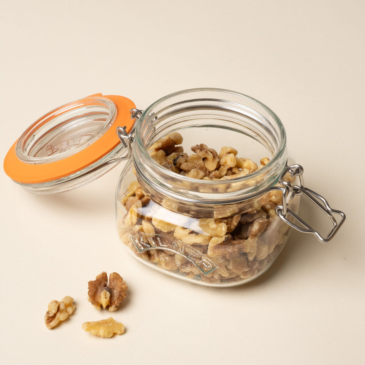 A shorter storage glass square jar filled with nuts and with an open top lid with a rubber seal and steel clip closure.