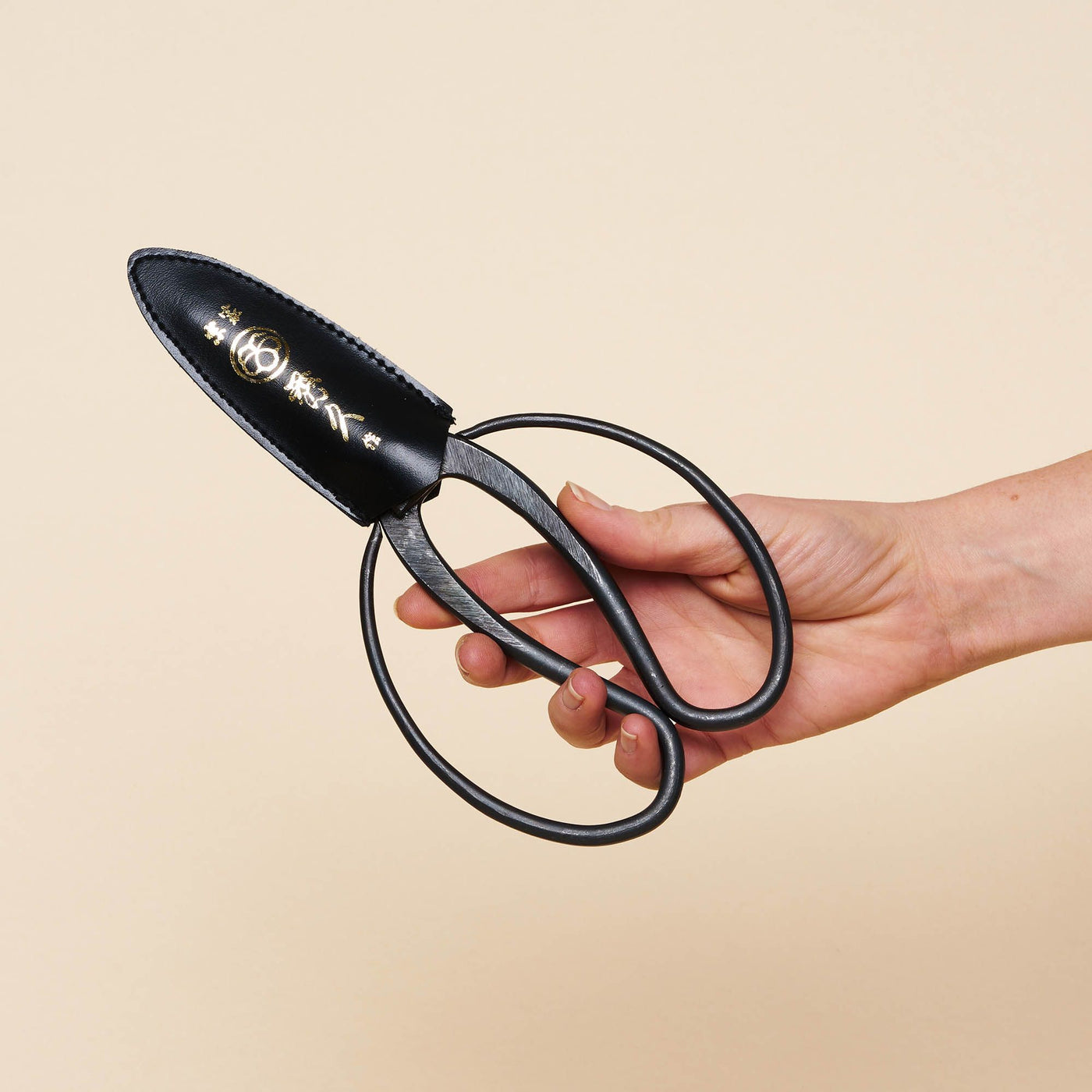 A hand holds a pair of Japanese Gardening Shears, with a black balloon-shaped handle.