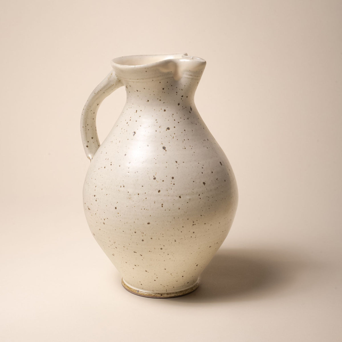 A hand-formed large classic ceramic pitcher with a spout and handle in a warm off-white color with iron speckles