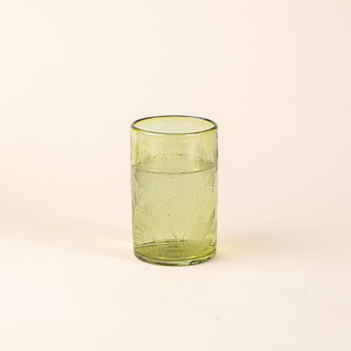 An olive tumbler glass made of recycled glass with etched thistle designs on it filled with water.
