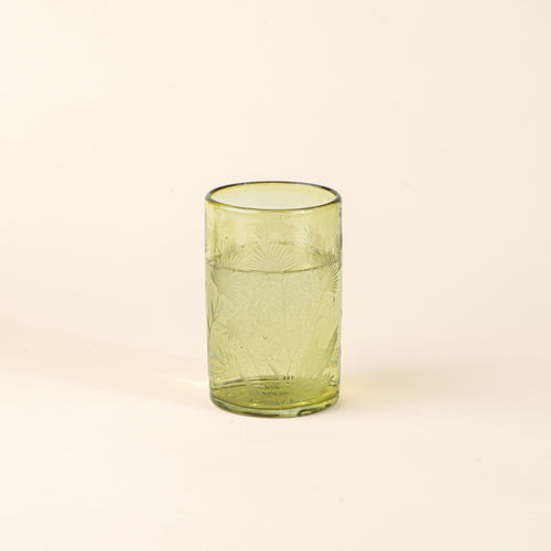 An olive tumbler glass made of recycled glass with etched thistle designs on it filled with water.