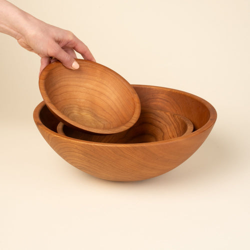 A hand holds out a small bowl to nestle in with a set of 3 cherry wood bowls.