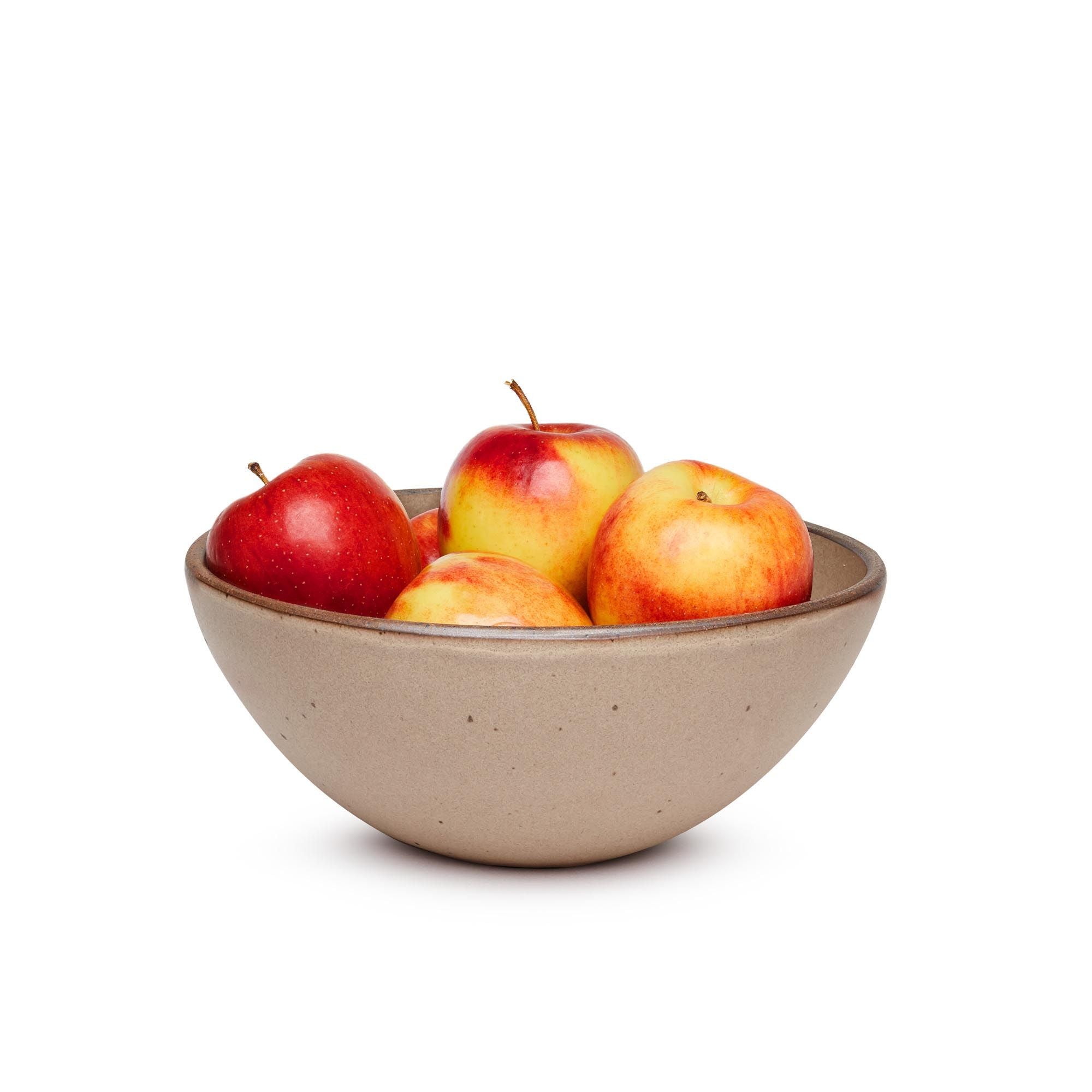 A large rounded ceramic bowl in a warm pale brown color featuring iron speckles and an unglazed rim, filled with apples