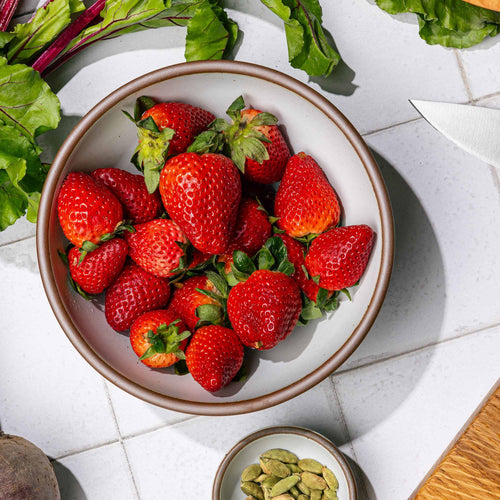 A dinner-sized shallow bowl filled with strawberries on a kitchen counter.