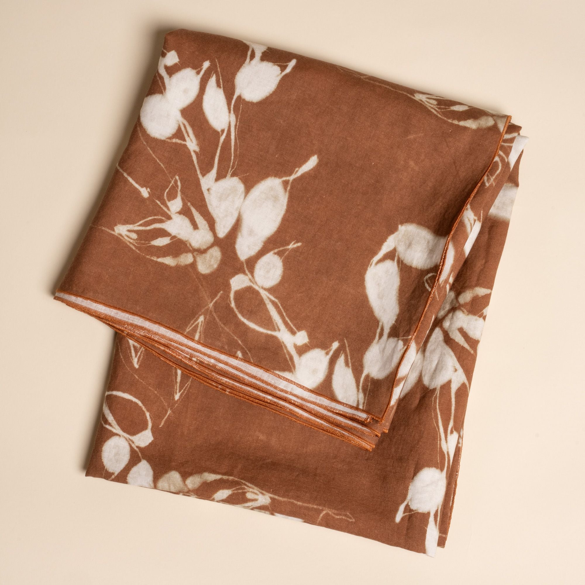 A folded tablecloth in a brown color with white botanical print on a neutral background.