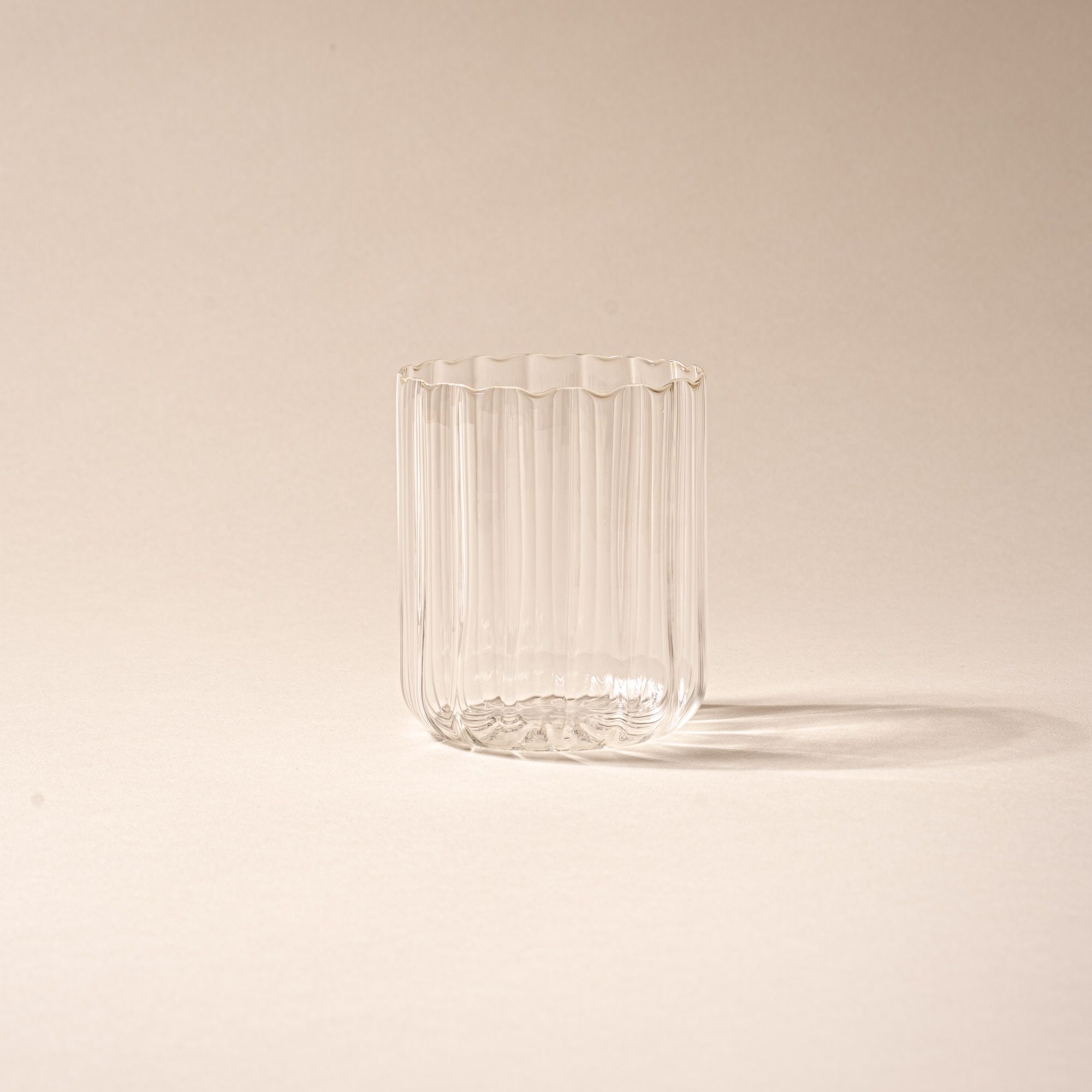 Empty ribbed glass tumbler casting a shadow on a neutral background.