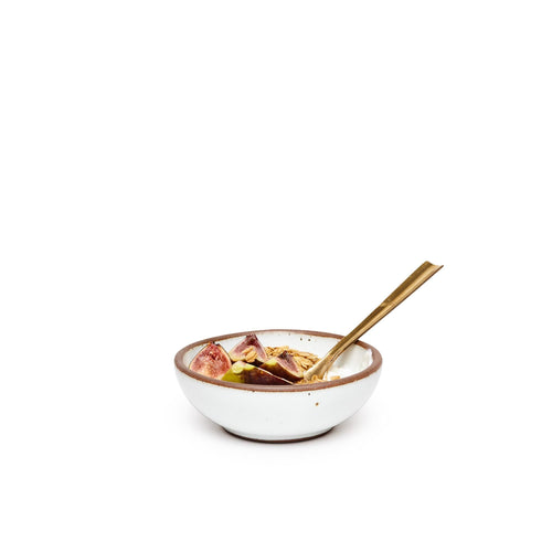 Yogurt and fruit with spoon in a small shallow ceramic bowl in a cool white color featuring iron speckles and an unglazed rim