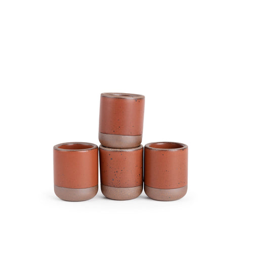 A set of 4 small, short ceramic mug cups in a cool burnt terracotta color featuring iron speckles and unglazed rim and bottom base, stacked in a row of 3, with the 4th on top.