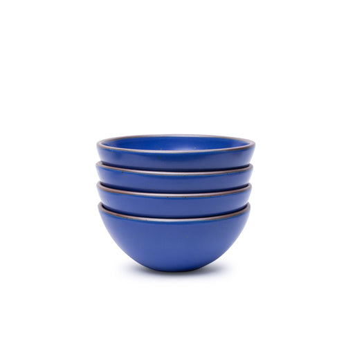 A stack of 4 medium rounded ceramic bowls in a cobalt blue color featuring iron speckles and an unglazed rim