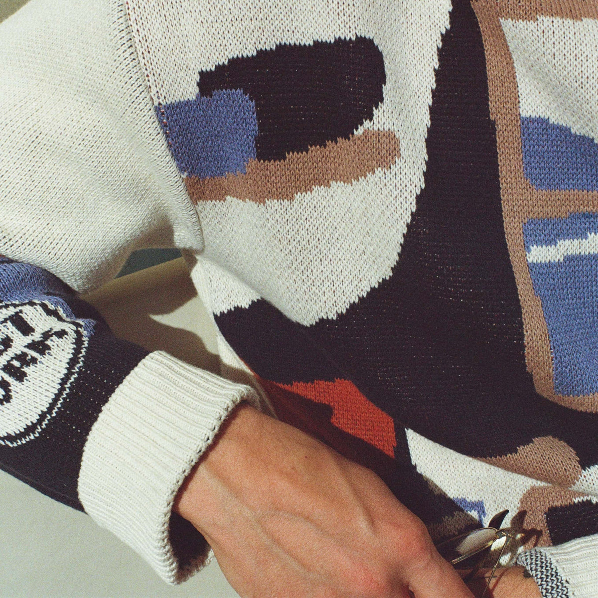 A closeup of a sweater with an illustration of a pottery workshop with a large window, shelves, and table with mugs and bowls. The sweater features cream, navy, terracotta, tan and blue colors.