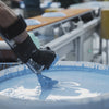 In a pottery factory, a pot is dipped into a bucket of glaze, and workers wiping off some glaze on the rim and botton base.