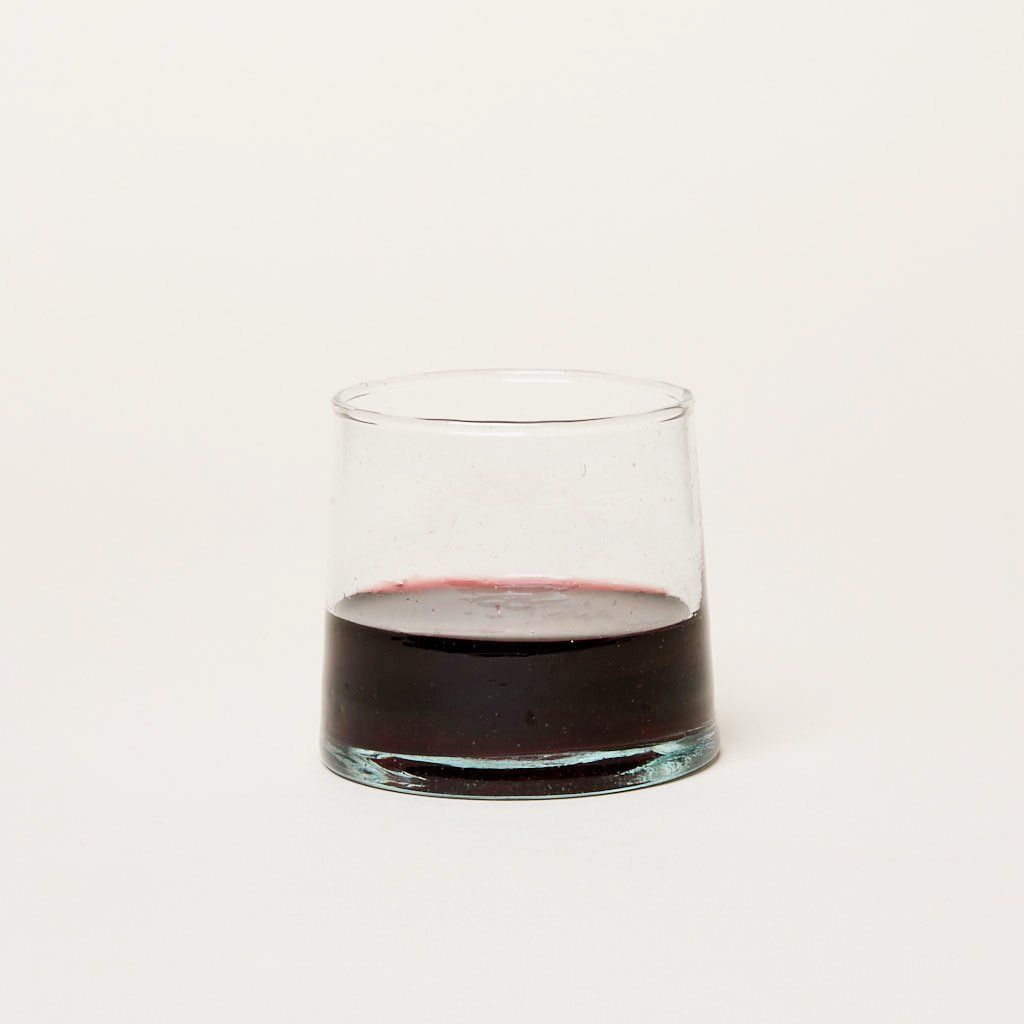 A short cylindrical drinking glass that flares slightly at the base, filled partly with red wine