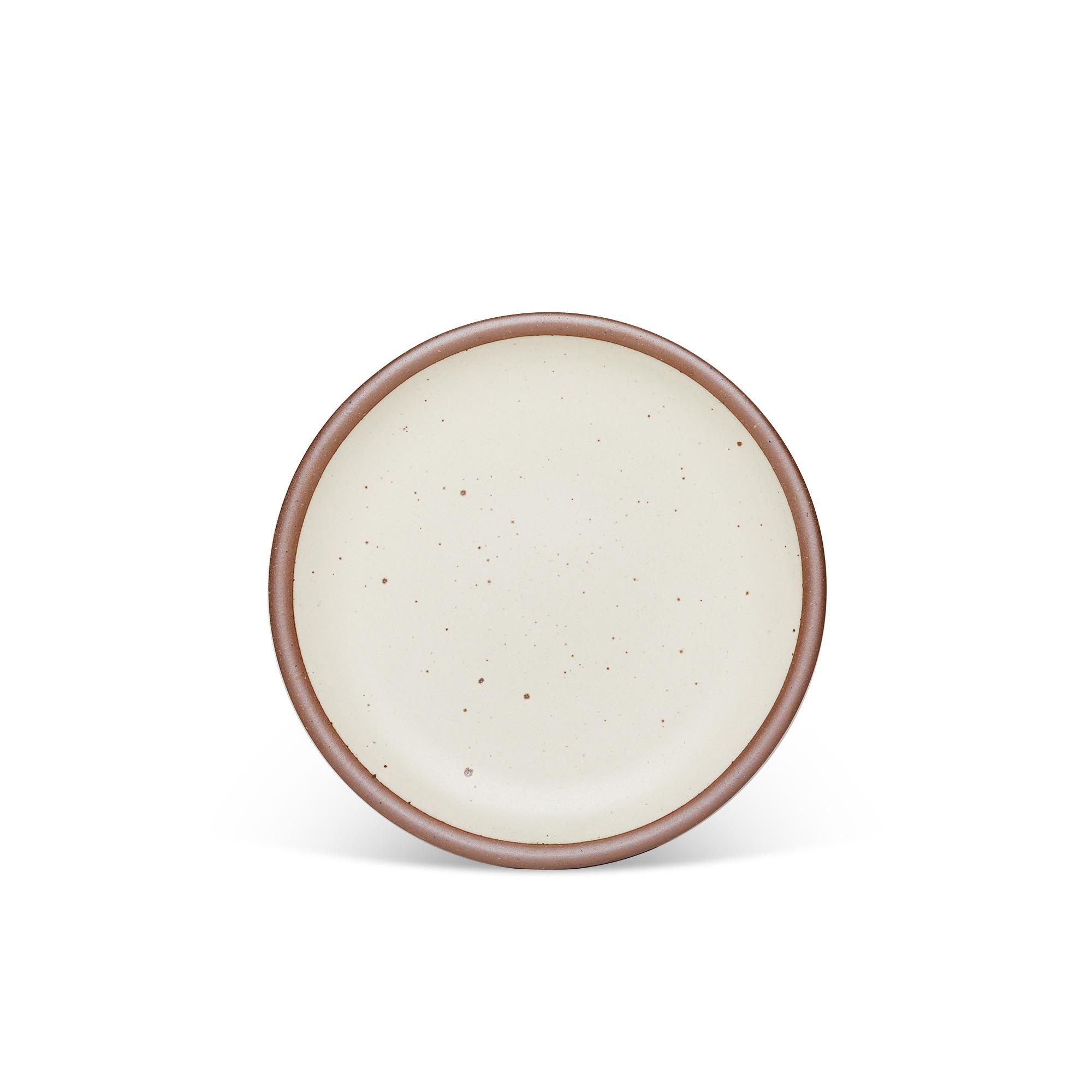A medium sized ceramic plate in a warm, tan-toned, off-whitecolor featuring iron speckles and an unglazed rim.