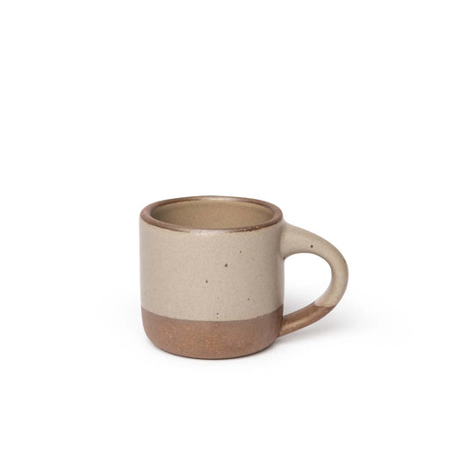 A small sized ceramic mug with handle in an pale warm brown glaze featuring iron speckles and unglazed rim and bottom base.