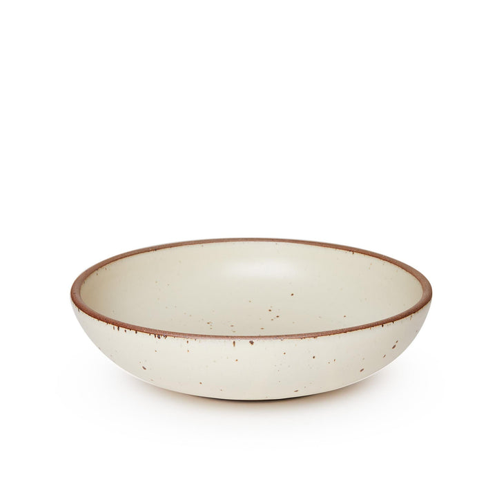 A large shallow serving ceramic bowl in a warm, tan-toned, off-white color featuring iron speckles and an unglazed rim.