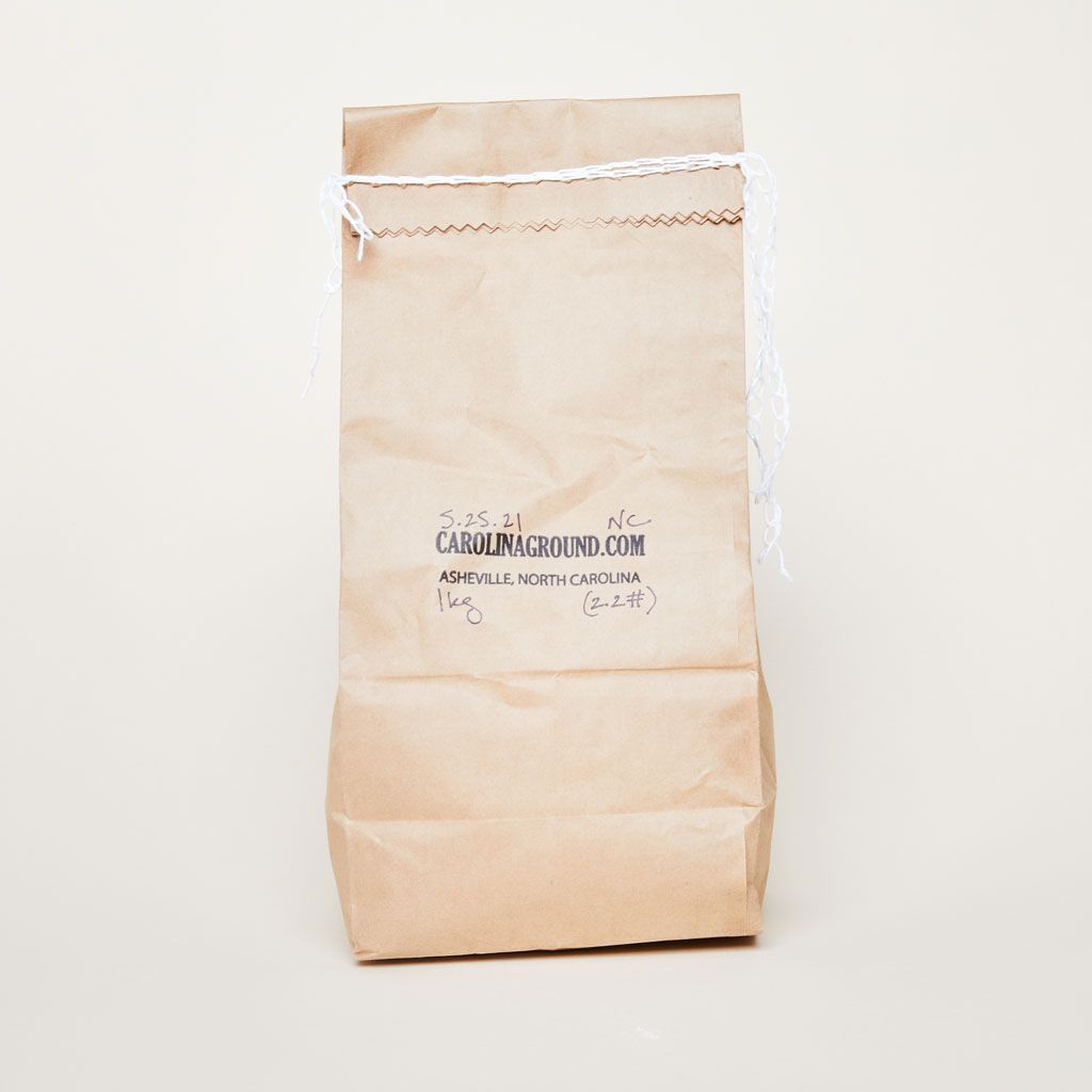 A brown paper bag stitched closed with white string at the top and "Carolinaground.com Asheville, North Carolina" stamped on it in black ink