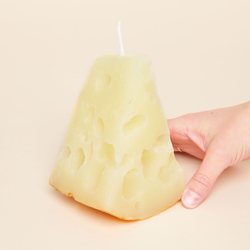 A triangular pale yellow candle with a texture that suggests gruyere cheese, held by a hand