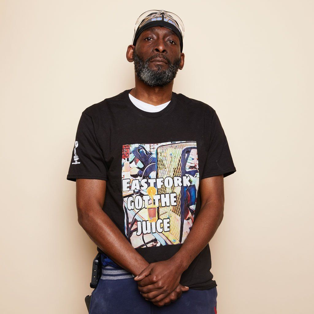 A person whose hands are folded at center waist wears a black Drip Life tee that reads "East Fork Got The Juice."